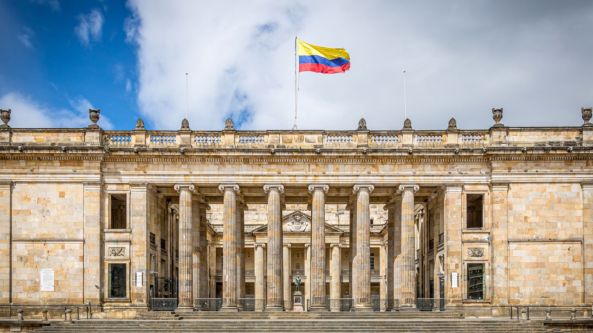 Front of Congress of Colombia building with flag waving on top below the sky.