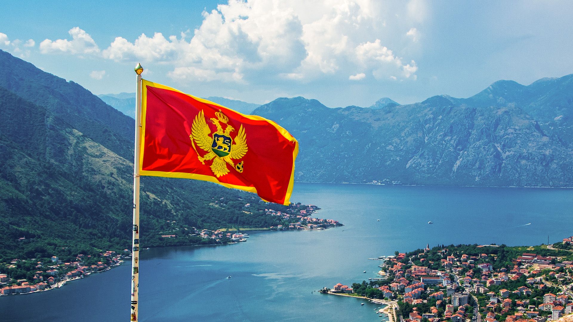 Montenegro flag waving in front of riverside and mountain landscape.